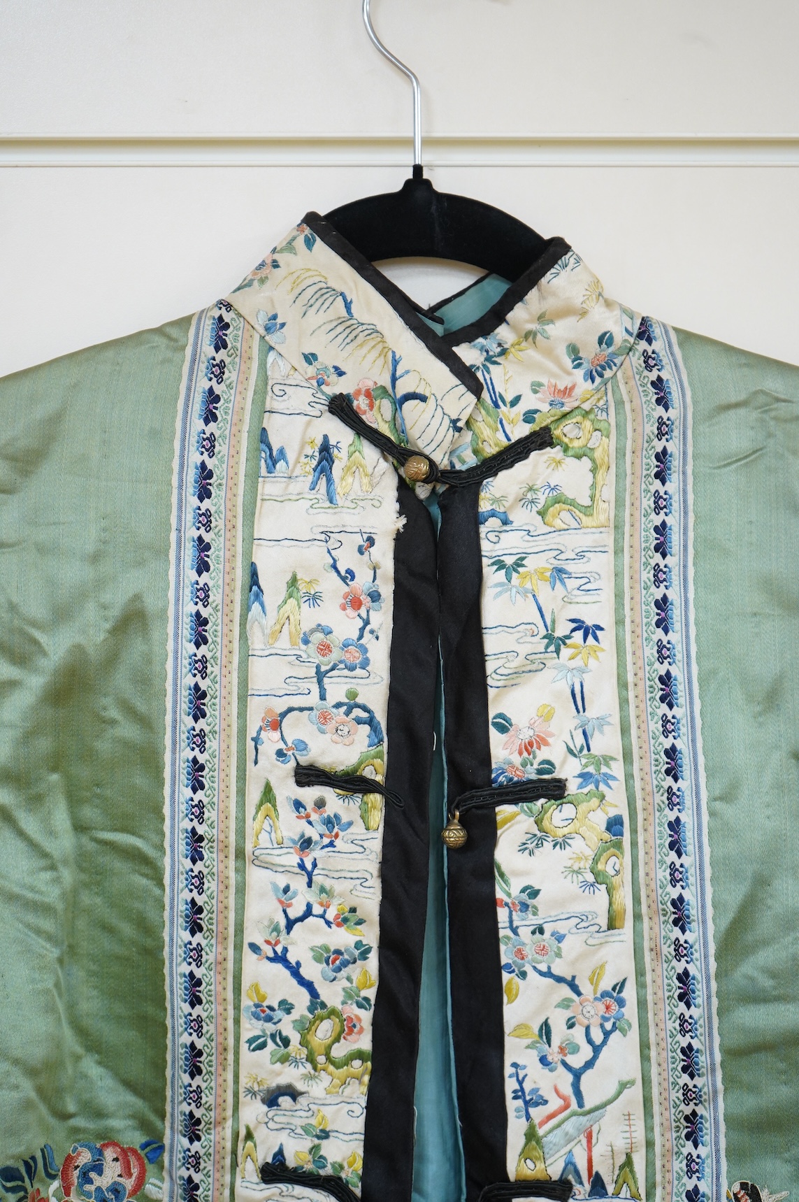 An early 20th century Chinese green silk polychrome embroidered jacket. Worked with Chinese knot embroidery and stem stitch into flowers, butterflies and bats, edged with woven silk ribbon and a figurative embroidered bo